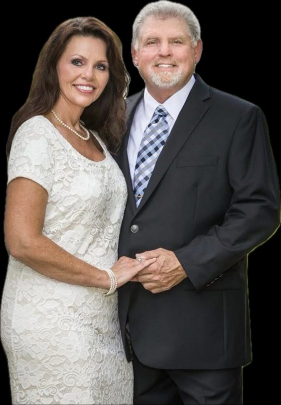 Ray Dotson in a dark suit and checked tie, holding hands with his wife, Lesa, who wears a white lace dress and pearls.