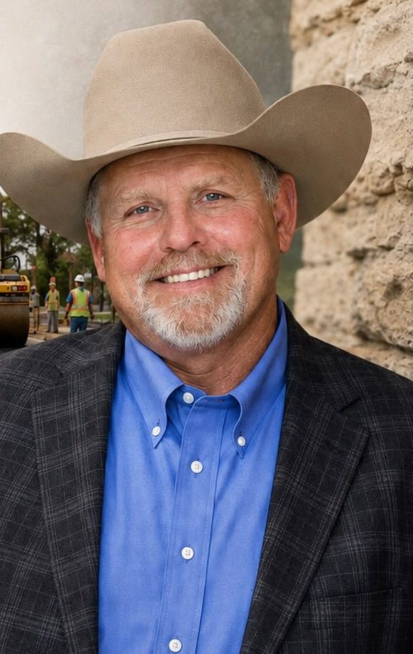 Ray Dotson in a cowboy hat and blazer, photographed in front of a road resurfacing crew at work.
